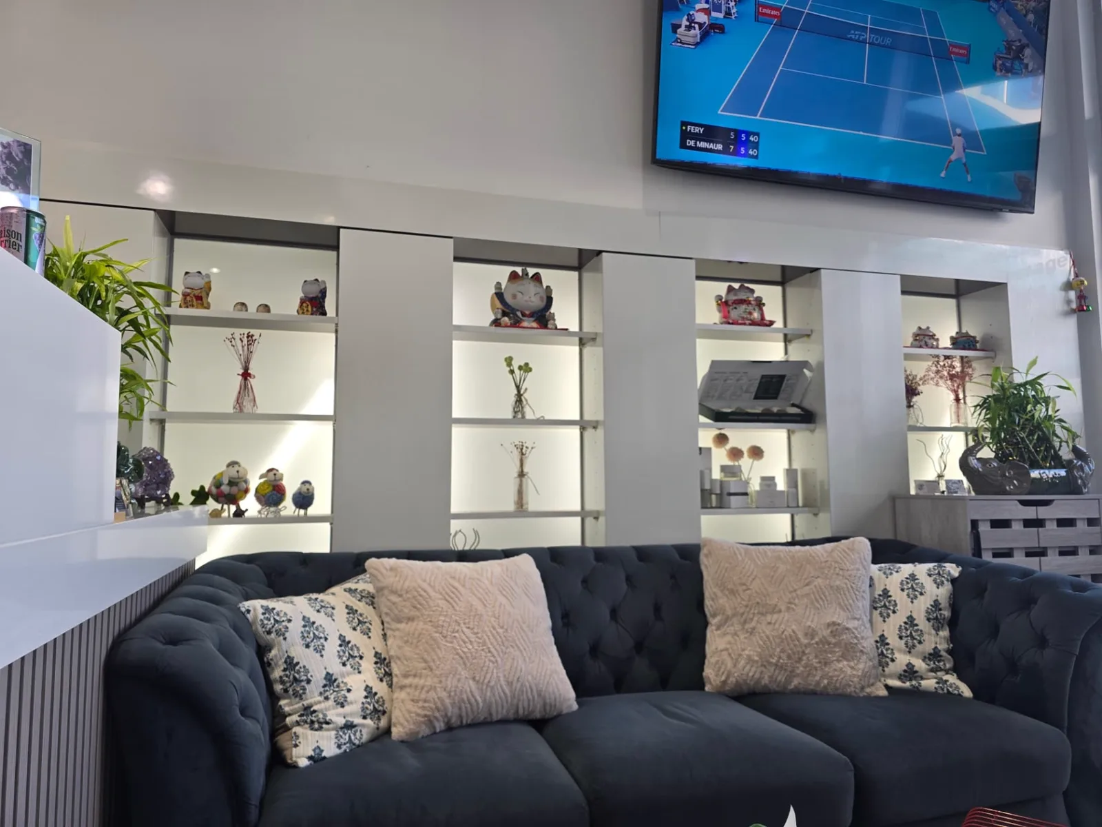 A deep blue tufted sofa with cushions in front of lit display shelves at Radiant Sun Wellness.