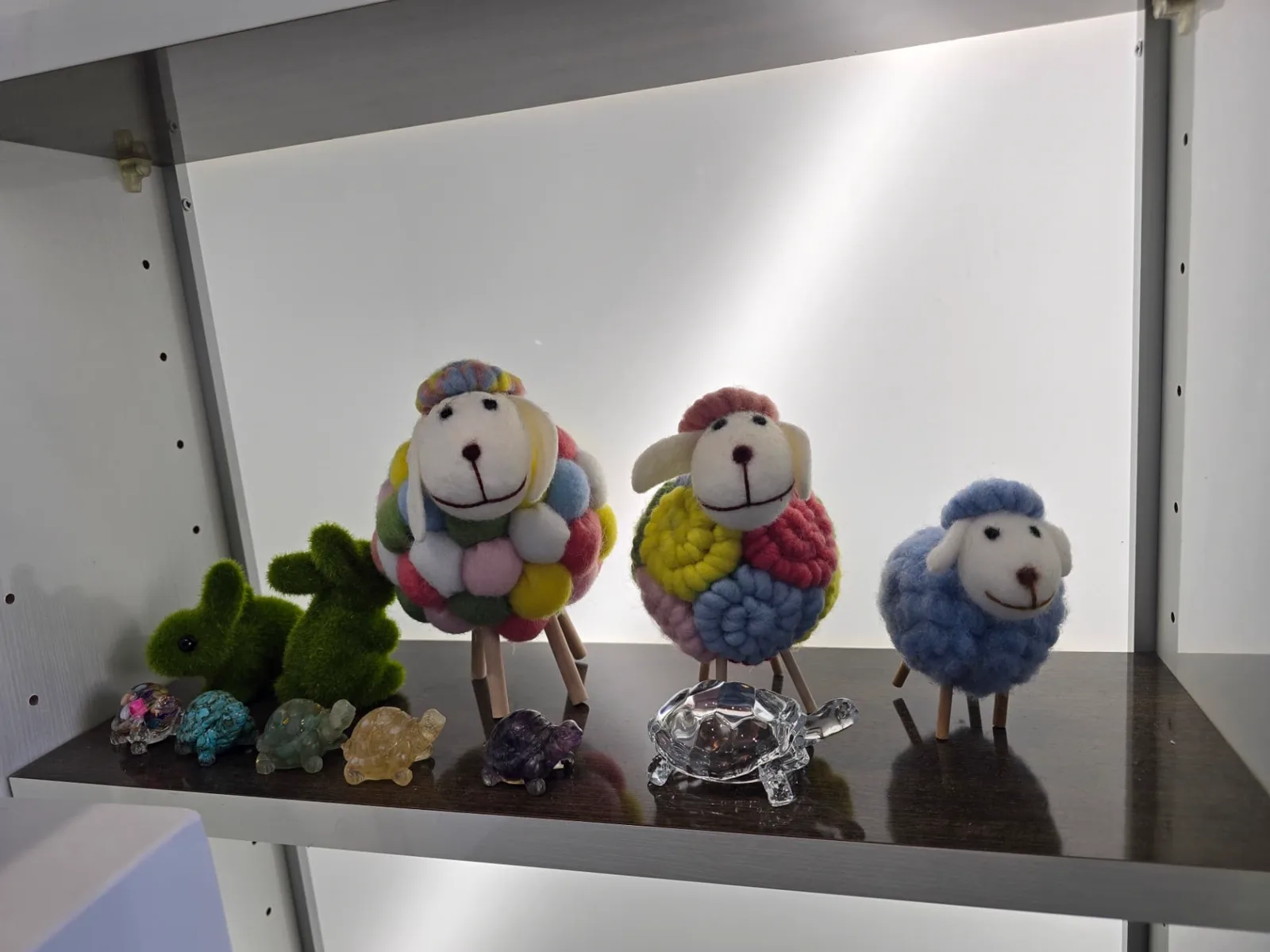 A lit shelf holding felted wool sheep, small moss rabbits and carved stone turtles.