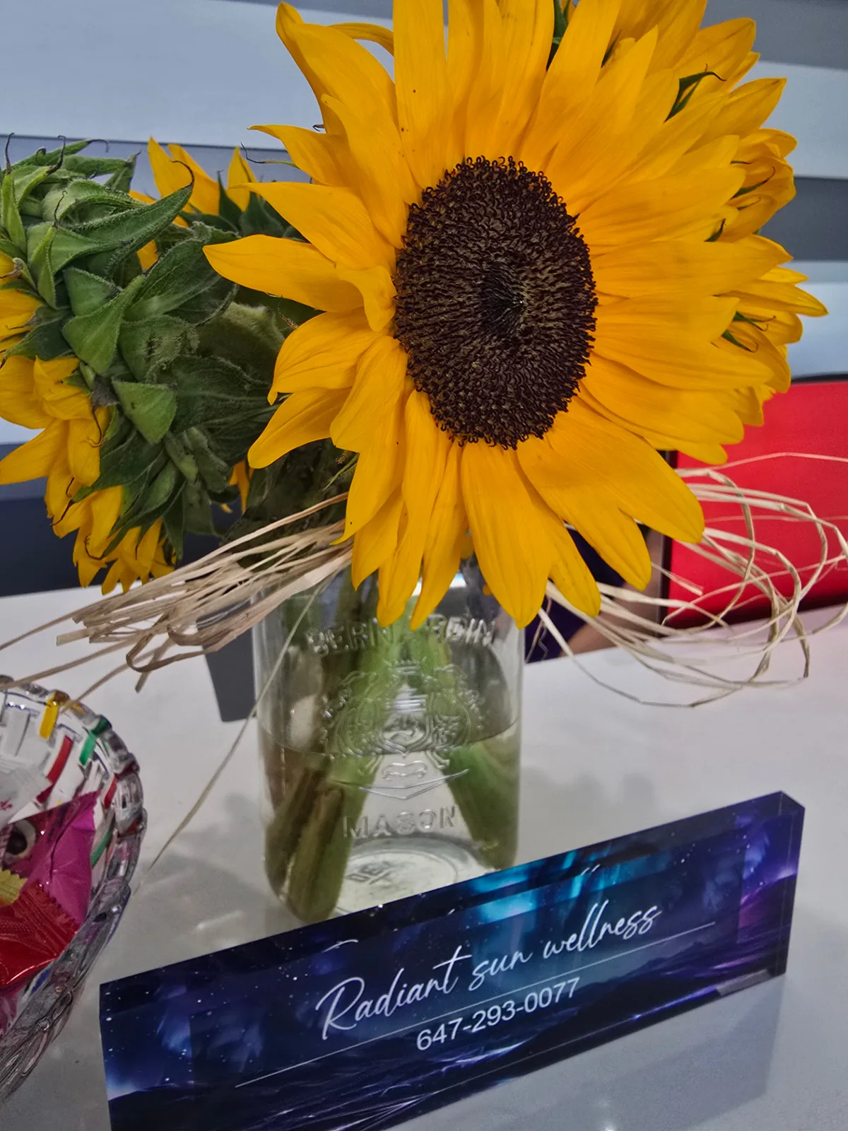 Fresh sunflowers in a glass jar beside the Radiant Sun Wellness desk plaque at reception.